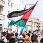 a crowd of people walking down a street holding flags